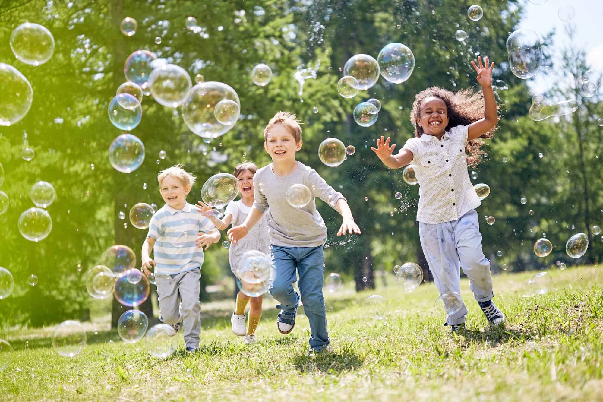 Children playing with bubbles outdoors in a sunny park, promoting fun, social interaction, and outdoor activity benefits.