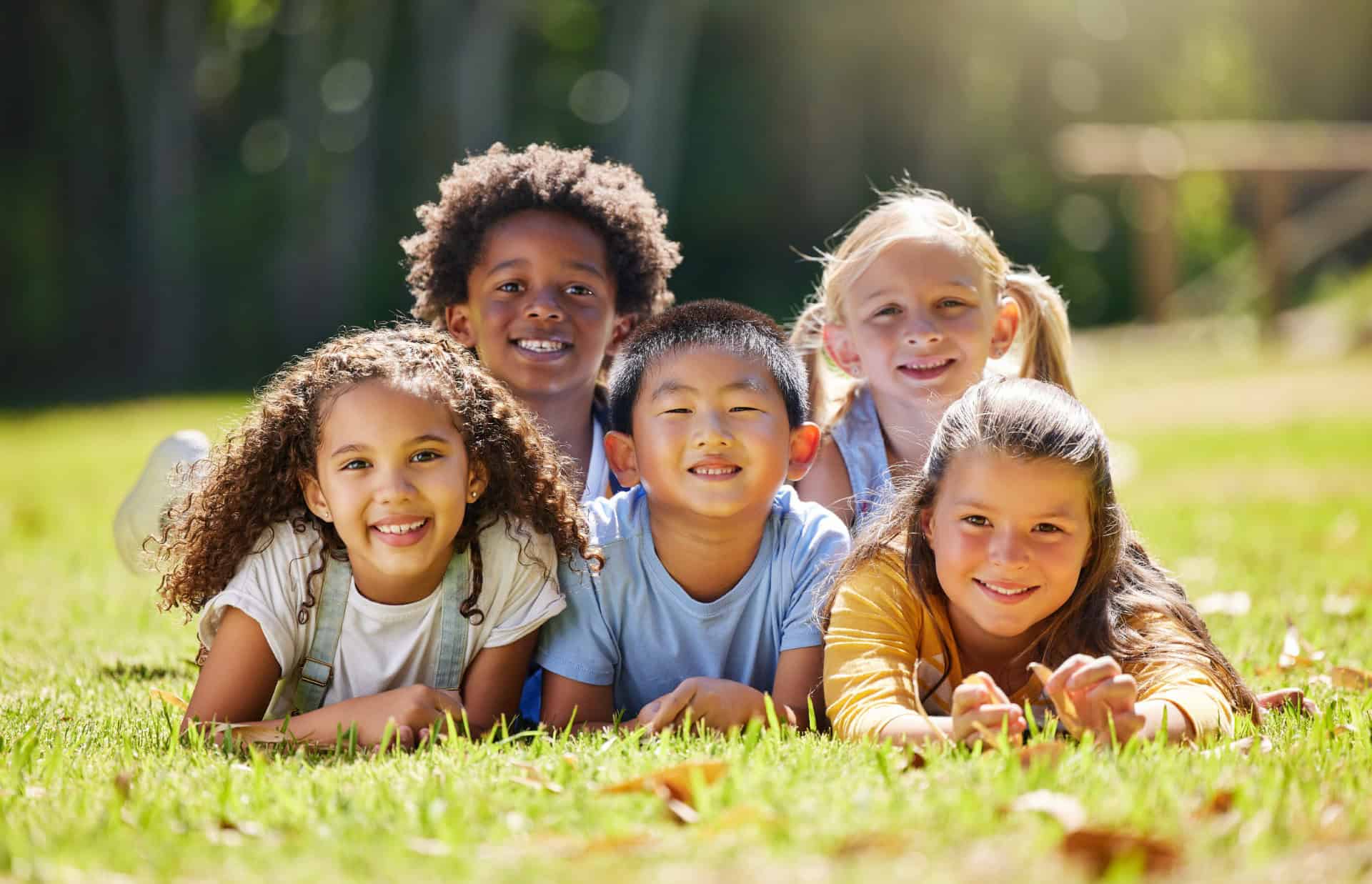 Colorful diverse children smiling and lying on grass outdoors, enjoying playtime, highlighting childhood happiness and social development.