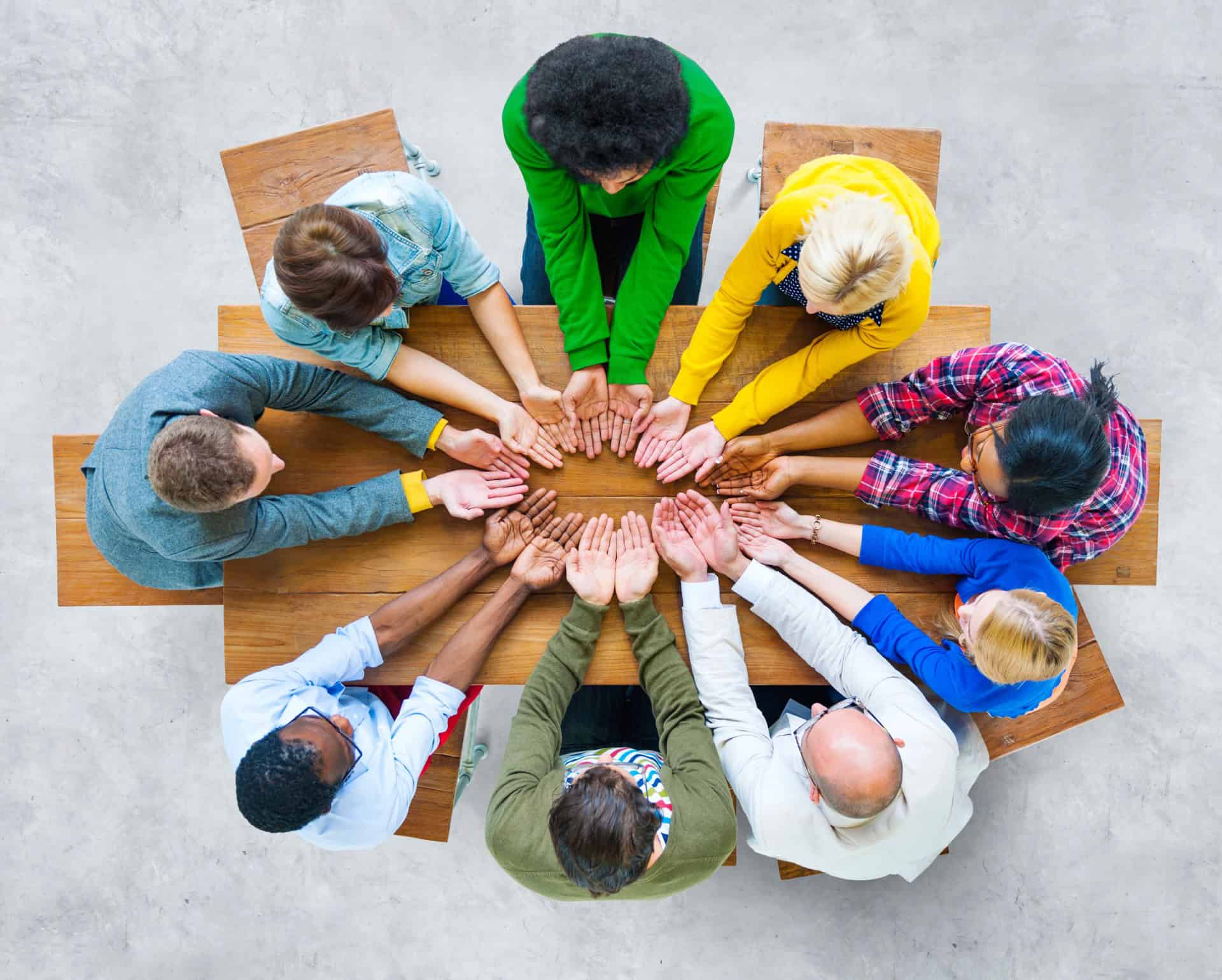 Diverse group of people creating a circle with hands for teamwork or support, emphasizing education and community.