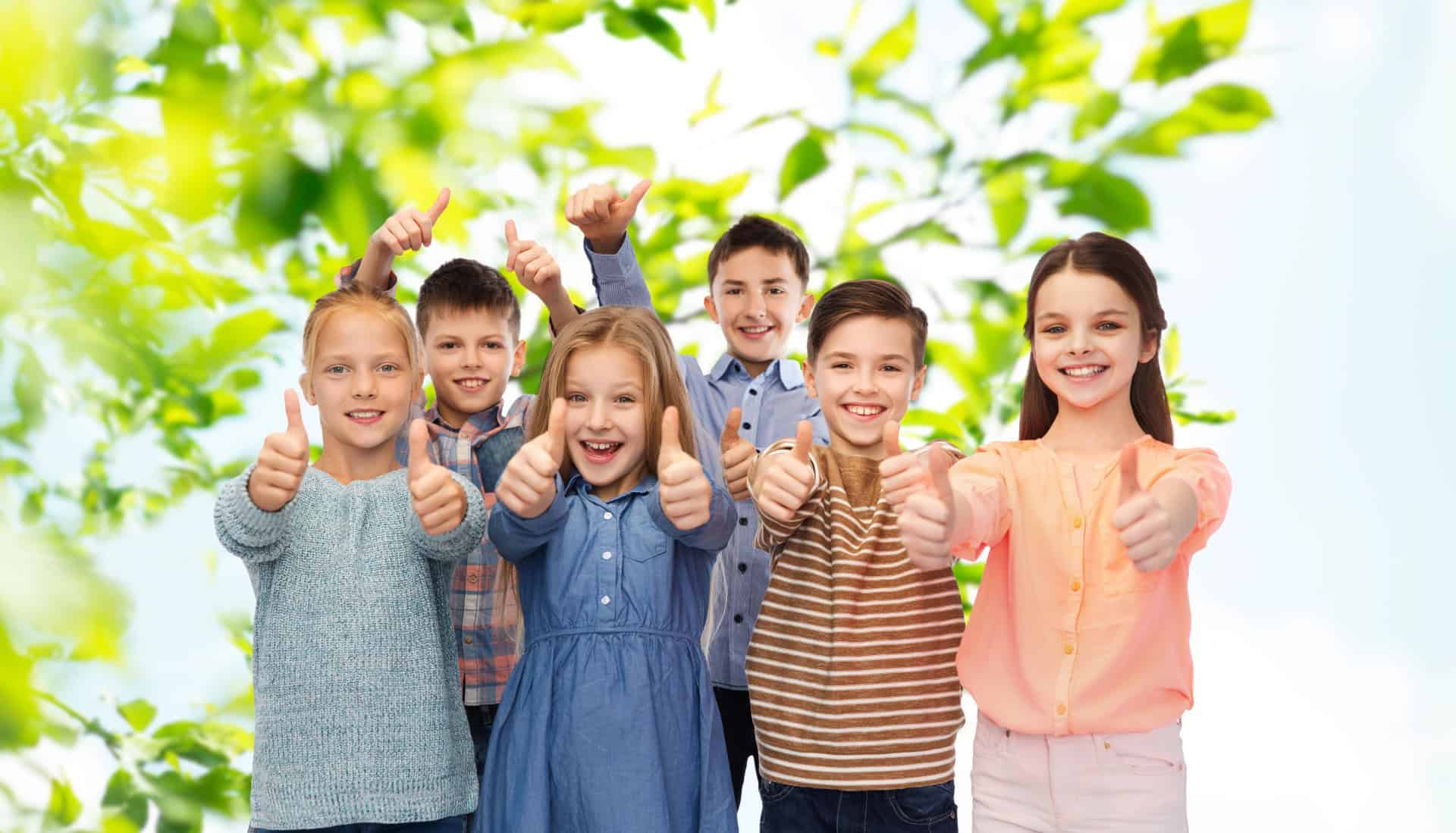 Happy children giving thumbs up outdoors, promoting positive school behavior and social skills.