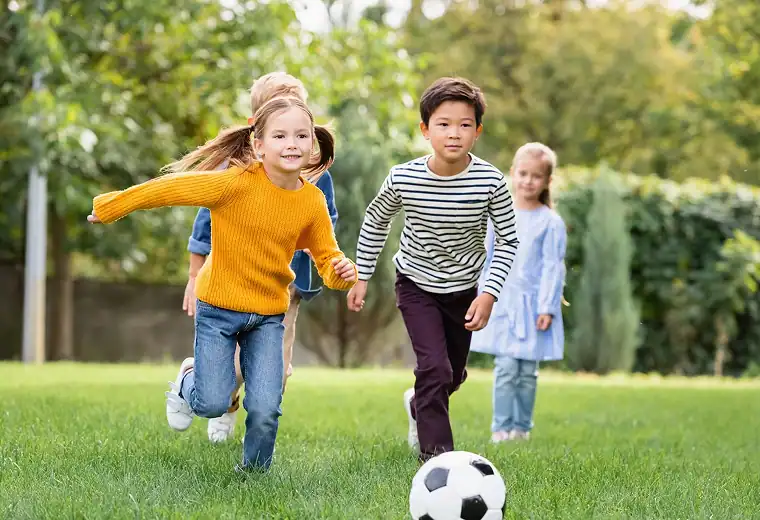 Young children playing soccer outdoors, promoting teamwork and physical activity.