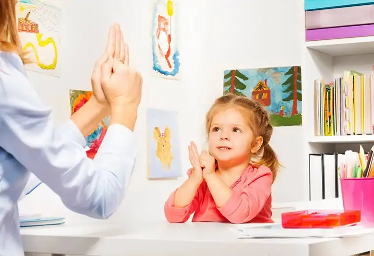 Bright young girl practicing positive behavior with therapist in a colorful therapy room.