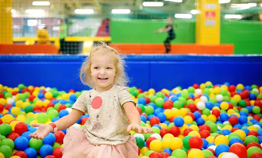 Bright smiling girl playing in colorful ball pit at Education Behavior Consultants.